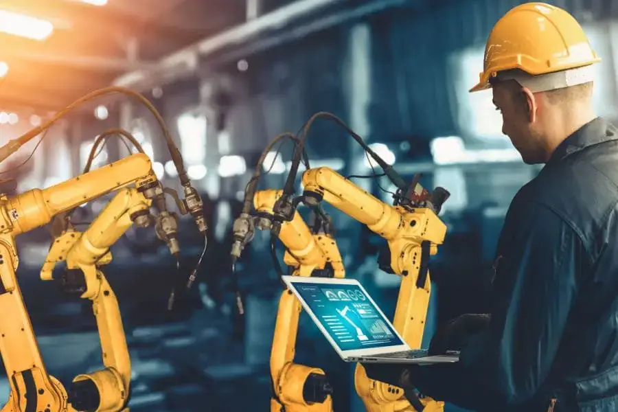 foto engenheiro de automação industrial segurando um laptop com dois braços robóticos a sua frente